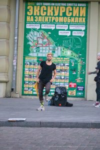Фотография мужчины с татуировками на руках, стоящего на фоне городской стены с картой Одессы. Современный стиль, уличная мода и динамичная атмосфера.