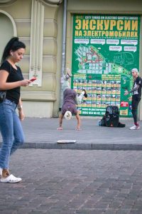 Фотография уличного акробата, выполняющего стойку на руках на фоне городской стены с афишами в Одессе. На руке видна татуировка.