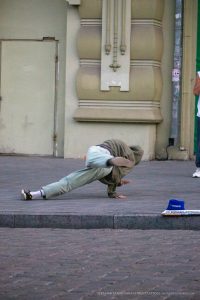 Фотография уличного акробата в динамичной позе. Задний фон представляет собой архитектурный элемент здания и карту города.
