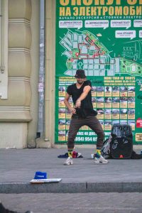 Фотография уличного мастера тату в Одессе, делающего татуировку клиенту на фоне городской стены с картой и афишами.