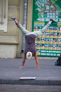 Фотография мужчины, выполняющего стойку на руках на фоне городской стены с картой Одессы. Татуировки на руках, спортивный стиль и динамичная поза.