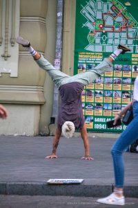 Фотография мужчины, выполняющего стойку на руках на фоне городской стены с картой Одессы. Татуировки на руках, спортивный стиль и динамичная поза.