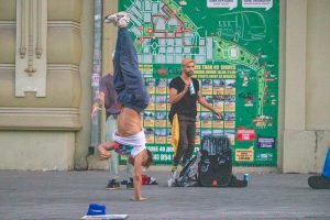 Фотография уличного акробата, выполняющего стойку на руках на фоне городской стены с картой и афишами. Яркий снимок для вдохновения на татуировки.