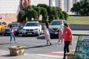 Фото: уличный фотограф делает снимки на фоне автомобилей и городской архитектуры. Динамичная сцена, отражающая современную уличную культуру.