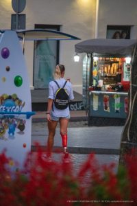 Фотография девушки, идущей по улице в шортах и рюкзаке. На девушке красные гетры и черный рюкзак.