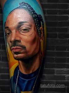 Фото тату реалистичного портрета Snoop Dogg на руке, выполненного в ярких цветах с использованием теней и световых эффектов.