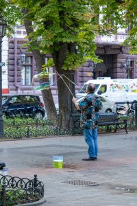 Фотография уличного артиста, создающего мыльные пузыри на фоне городской улицы и деревьев.