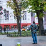 Фотография уличного артиста, делающего мыльные пузыри в городском парке. На заднем плане деревья, фонари и прохожие.