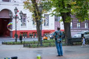 Фотография уличного артиста, делающего мыльные пузыри в городском парке. На заднем плане деревья, фонари и прохожие.