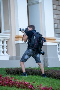 Фотография профессионального фотографа, снимающего уличную татуировку. Он одет в повседневную одежду и несет профессиональное фотооборудование.