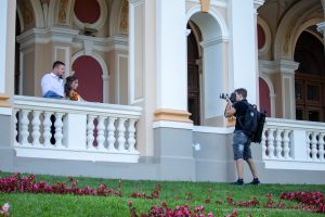 Фотография фотографа, снимающего пару молодоженов на фоне красивого здания. Видна татуировка на руке фотографа.