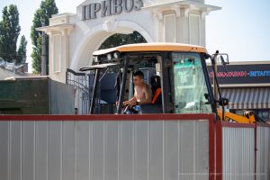 Фотография мужчины, сидящего в кабине спецтехники, с татуировкой на плече и предплечье. Видна татуировка на руке.