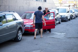 Фотография мужчины, открывающего дверь красного автомобиля, с видимой татуировкой на ноге.