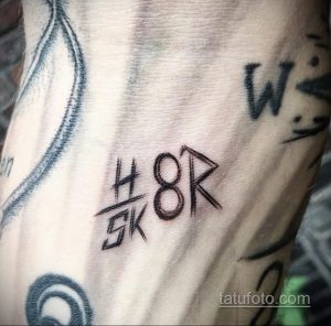 Фото тату с аббревиатурой 'H8R' и черными штрихами на руке. Простой, лаконичный дизайн, выполненный черными чернилами.