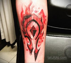 Фото тату символа Орды из World of Warcraft, выполненного в технике акварели с использованием красных и черных оттенков на предплечье.