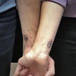 Фото тату на запястьях пары: стилизованные изображения половинок авокадо, вместе образующих целое. Минималистичный дизайн, выполненный в черном цвете с небольшими зелеными акцентами.