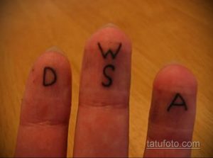 Фотография татуировок в виде отдельных букв 'D', 'W', 'S' и 'A', выполненных на пальцах рук. Простой и лаконичный дизайн.