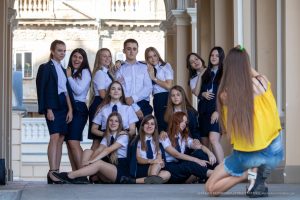 Группа студентов в школьной форме позирует для уличного фотографа на фоне красивого здания.