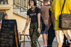 Фотография стильной девушки с короткой стрижкой и татуировкой волка на руке. Девушка одета в черную футболку и камуфляжные брюки.