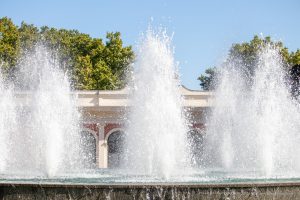 Фотография фонтана с брызгами воды на фоне голубого неба и зелени. Идеальный фон для поиска идей для тату.