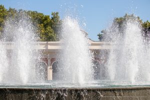 Фотография фонтана с брызгами воды на фоне голубого неба и зелени. Идеальный фон для поиска идей для тату.
