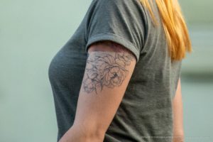Фото тату: детальный рисунок пиона в стиле лайнуорк на плече. Черно-белая татуировка с плавными линиями и реалистичным изображением цветка.