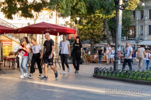 Фото городской улицы с людьми, у некоторых из которых видны татуировки на руках. Оживленная атмосфера, современный стиль.