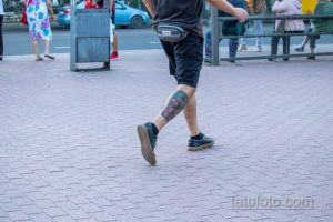 Фото тату на голени мужчины, идущего по улице. Рисунок изображает яркую композицию с элементами в стиле традиционной татуировки.