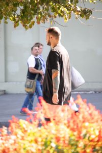 Фото мужчины с татуировкой карпа кои на предплечье. Мужчина идет по улице, татуировка хорошо видна на фоне одежды и листвы.