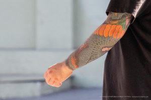 Фото тату: рука мужчины с татуировкой карпа кои в ярких цветах. Детализированный рисунок и динамичная композиция.