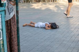 Фотография: маленький ребенок лежит на тротуаре, рядом женщина и прохожие на улице.