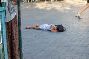 Фотография: маленький ребенок лежит на тротуаре, рядом женщина и прохожие на улице.