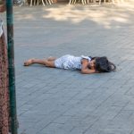 Фотография: маленький ребенок лежит на тротуаре, рядом женщина и прохожие на улице.