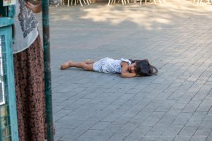 Фотография: маленький ребенок лежит на тротуаре, рядом женщина и прохожие на улице.