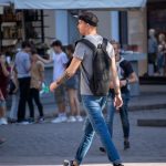 Фото мужчины с татуировкой на руке, идущего по улице в окружении людей. Рисунок татуировки выполнен в реалистичном стиле с изображением автомата.