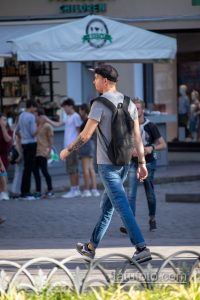 Фото мужчины с татуировкой на руке, идущего по улице в окружении людей. Рисунок татуировки выполнен в реалистичном стиле с изображением автомата.