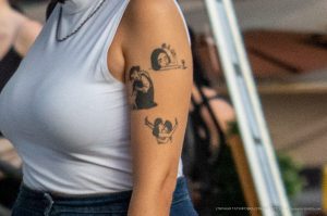 Фото тату на плече: три небольших черно-белых рисунка, изображающих лицо, фигуру и абстрактный символ, выполненные в минималистичном стиле.