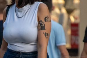 Фото тату на плече: небольшая черно-белая татуировка с изображением лица, расположенная на плече девушки.