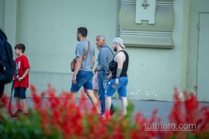 Фото тату на руке мужчины, идущего по улице. Видна часть татуировки в стиле графика, выполненной черными чернилами.