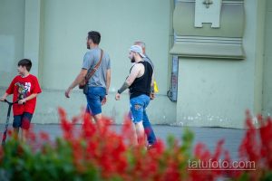 Фото тату на руке мужчины, идущего по улице. Видна часть татуировки в стиле графика, выполненной черными чернилами.