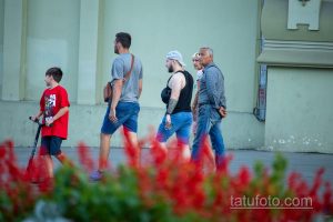 Фото тату на руке мужчины, идущего по улице. Видна часть татуировки в стиле графика, выполненной черными чернилами.