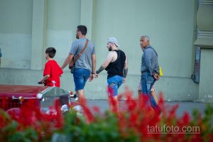 Фото тату на руке мужчины, идущего по улице с семьей. Видна часть татуировки в стиле графика, выполненной черными чернилами.