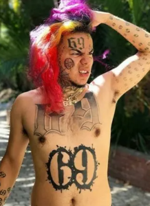 6ix9ine демонстрирует татуировки на груди, животе и руках, включая большие цифры '69' и детализированные рисунки.