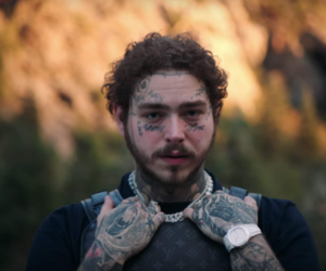 Фотография Post Malone с обширными татуировками на лице, шее, руках и груди. Видны изображения черепов, цветов и надписей.