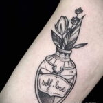 Фото тату: черно-белый рисунок бутылочки с цветами, внутри надпись 'self.love'. Минималистичный стиль.