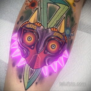 Фото тату: рисунок Маски из Zelda: Majora's Mask на руке с добавлением неонового свечения, выполненный в ярких цветах.