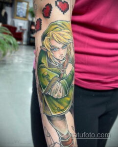 Фото тату на руке с изображением Линк из The Legend of Zelda в зеленом плаще, выполненное в реалистичном стиле.
