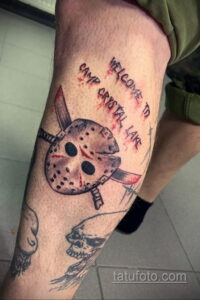 Фото тату Джейсона Вурхиза на ноге с надписью "Welcome to Camp Crystal Lake". Реалистичный стиль, черно-белая гамма, брызги крови. Идеально для фанатов фильмов ужасов.