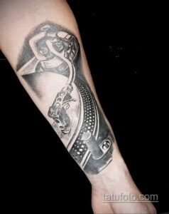 Фото тату на руке: реалистичное изображение диджейского проигрывателя с девушкой, танцующей рядом. Детализированный рисунок татуировки в черно-серых тонах.
