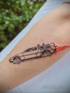 Черно-белое фото тату DeLorean из фильма 'Назад в будущее' на предплечье. Изображение выполнено в графичном стиле с добавлением красных языков пламени.